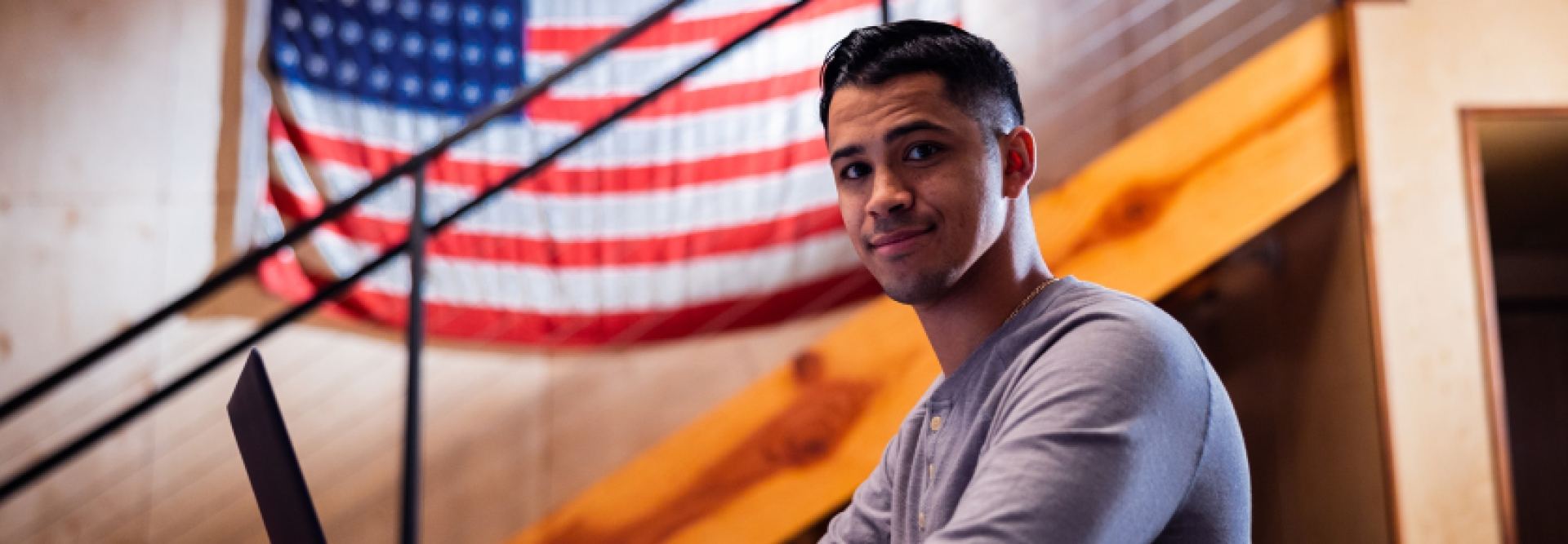 person in long sleeve shirt sitting at desk with american flag behind