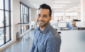 man in large open office setting smiling into camera