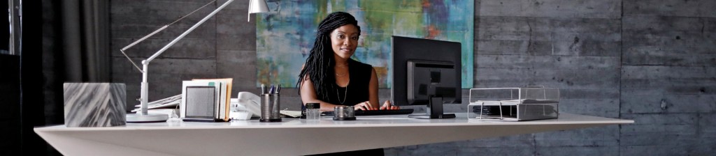 woman with long braids types on a computer at a huge white desk