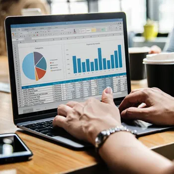 closeup on hands at a laptop keyboard. the laptop shows a pie chart and bar graph with data underneath