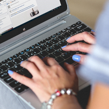 woman with blue painted nails types on a laptop keyboard