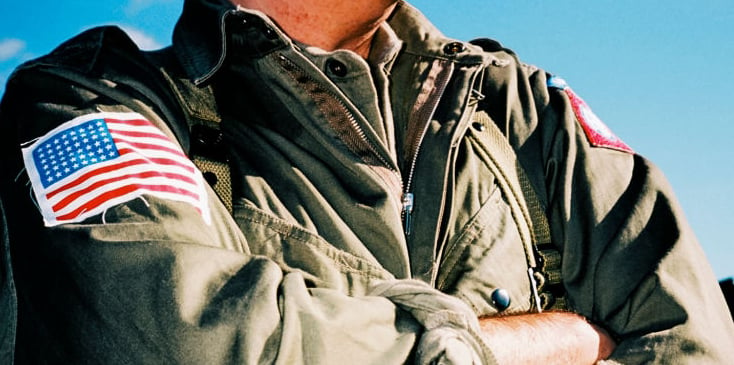 close up of a man wearing a U.S military jacket and folding his arms