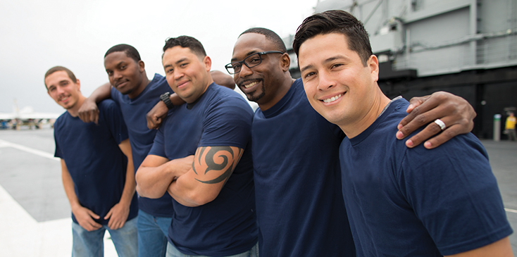 five male military servicemembers stand with their arms around each other's shoulders
