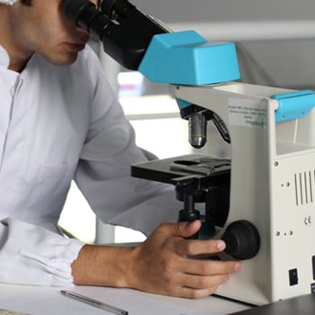 man in a white coat looks through a microscope