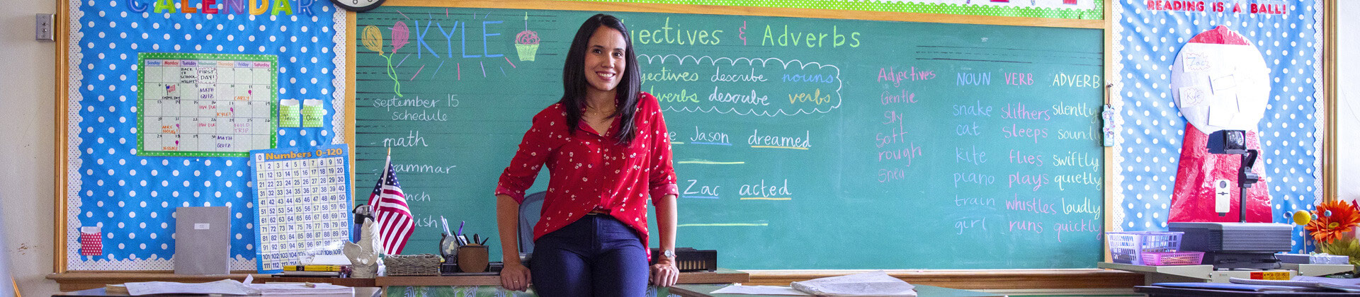 Abigail J. stands in front of a chalkboard  in her classroom
