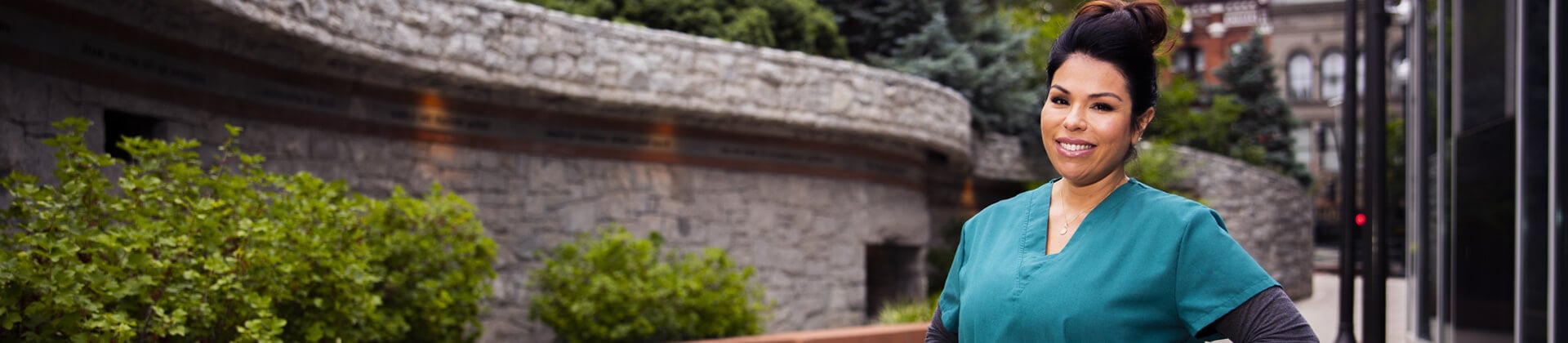 Lorena S. wears teal scrubs and stands in front of a building