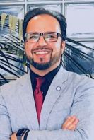 Monir Masoud crosses his arms while wearing a light gray suit and red tie