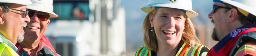 four people in hard hats and hi visibility vests talk onsite