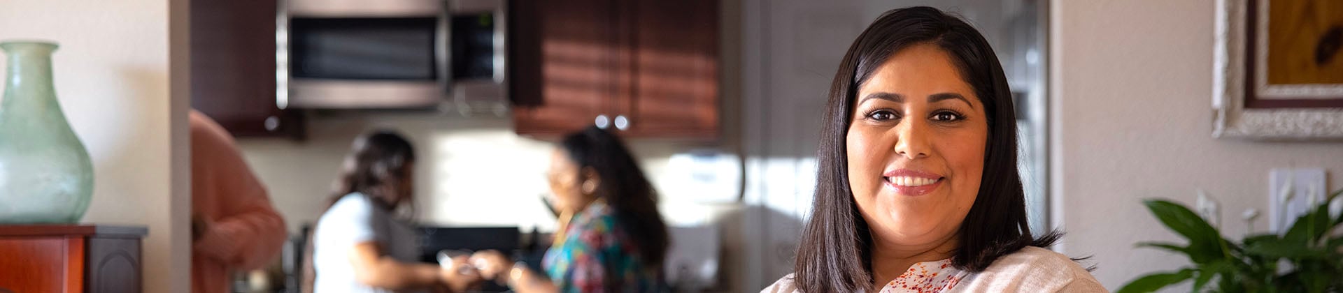 Closeup of Elizabeth V., Class of 2023, standing in a kitchen. There are two other women in the background talking