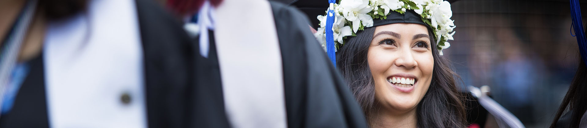  A woman with a graduation cap decorated with white flowers, stands in line to receive her diploma