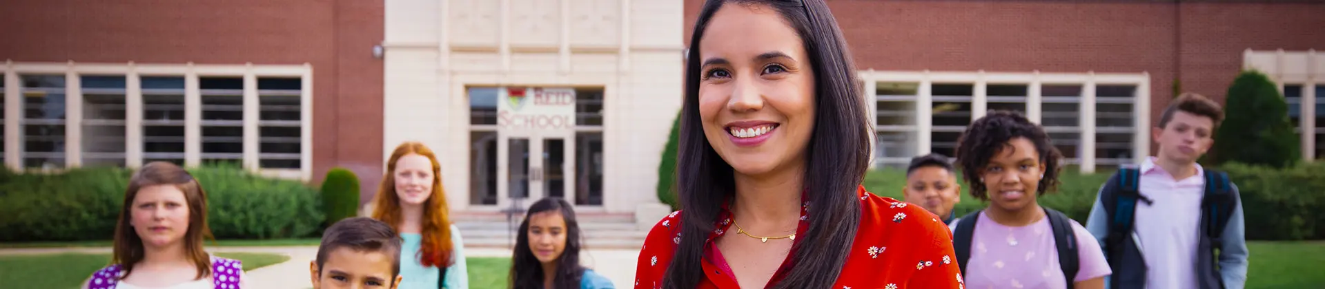 Abigail J. smiles in front of Reid School with students in the background.