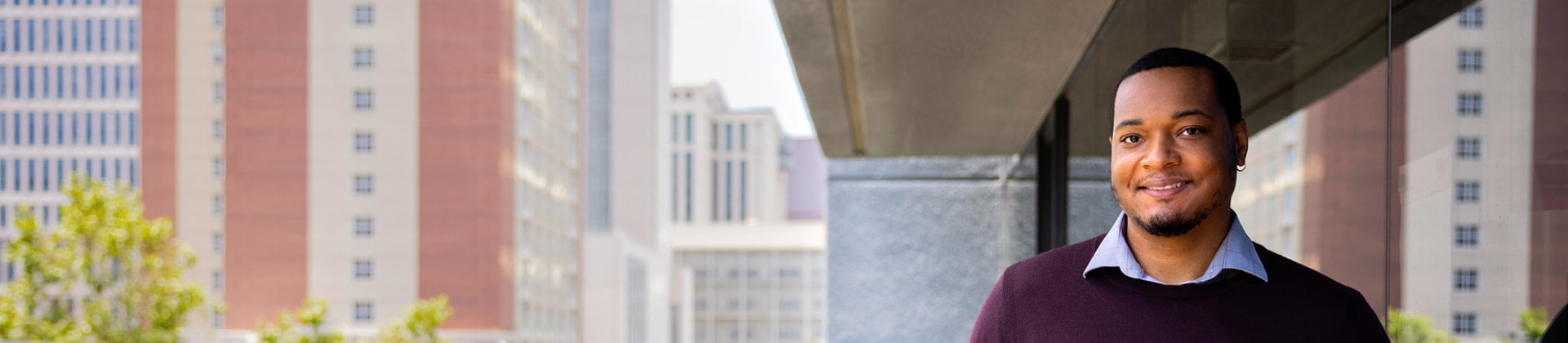 Â Man with a goatee and sweater stands under an awning at National University