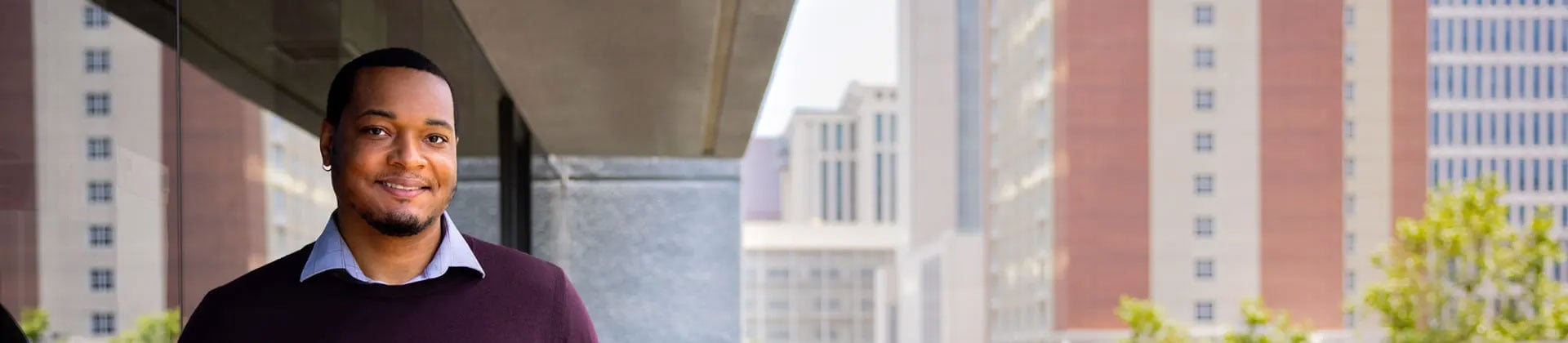 man outside with buildings behind him smiling at camera