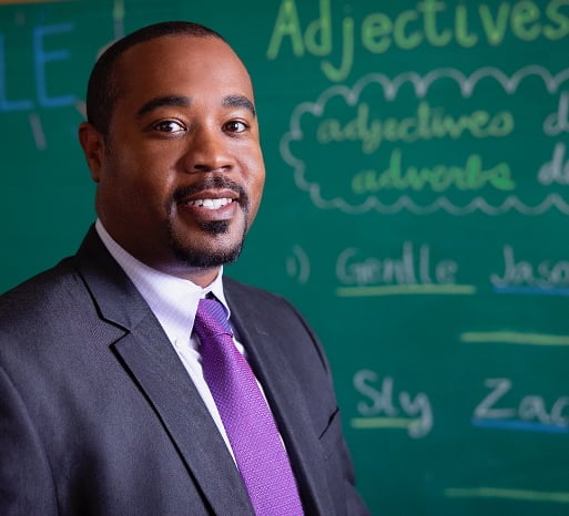 Man in a suit stands in front of a chalkboard