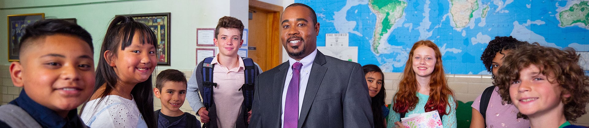 Prince M., Class of 2016, stands with a group of students. He wears a dark suit and purple tie.