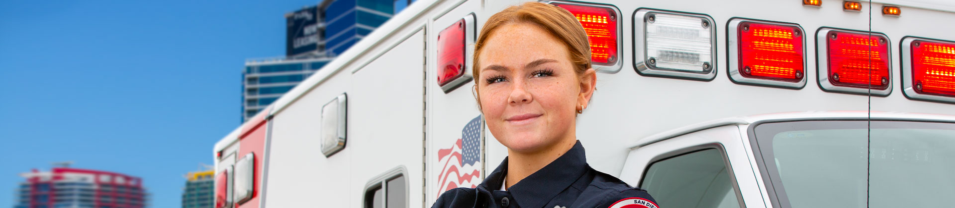 A woman with auburn hair pulled back stands in front of an ambulance 