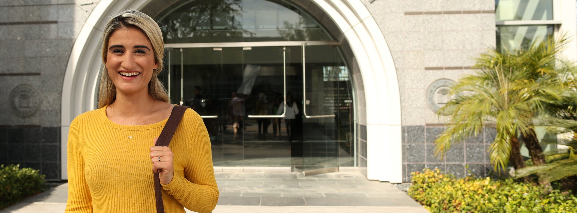 Woman with blonde hair wearing a yellow sweater stands in front of an NU campus building