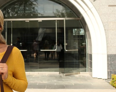 woman smiling with shoulder bag in front of national university building