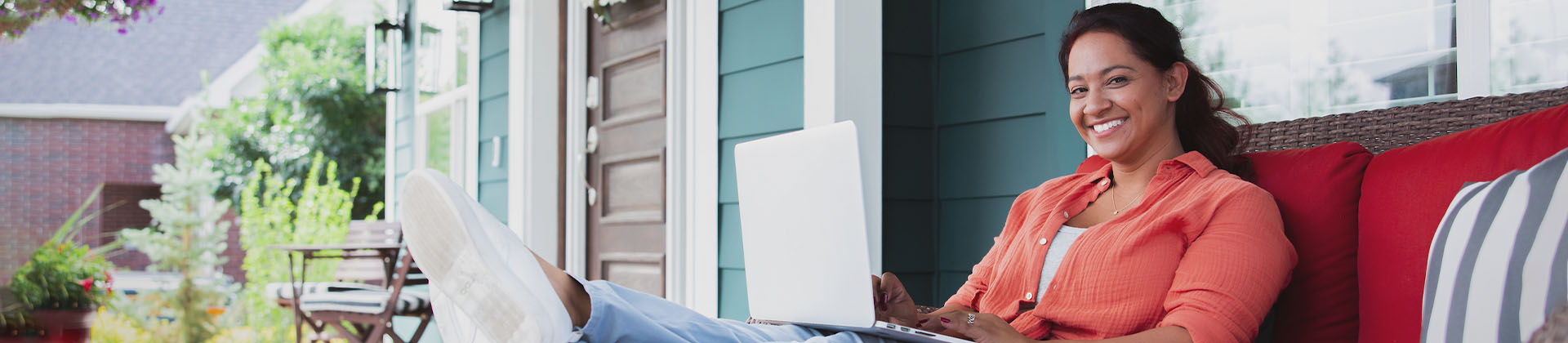 Woman with hair tied back sits on a porch with a laptop computer
