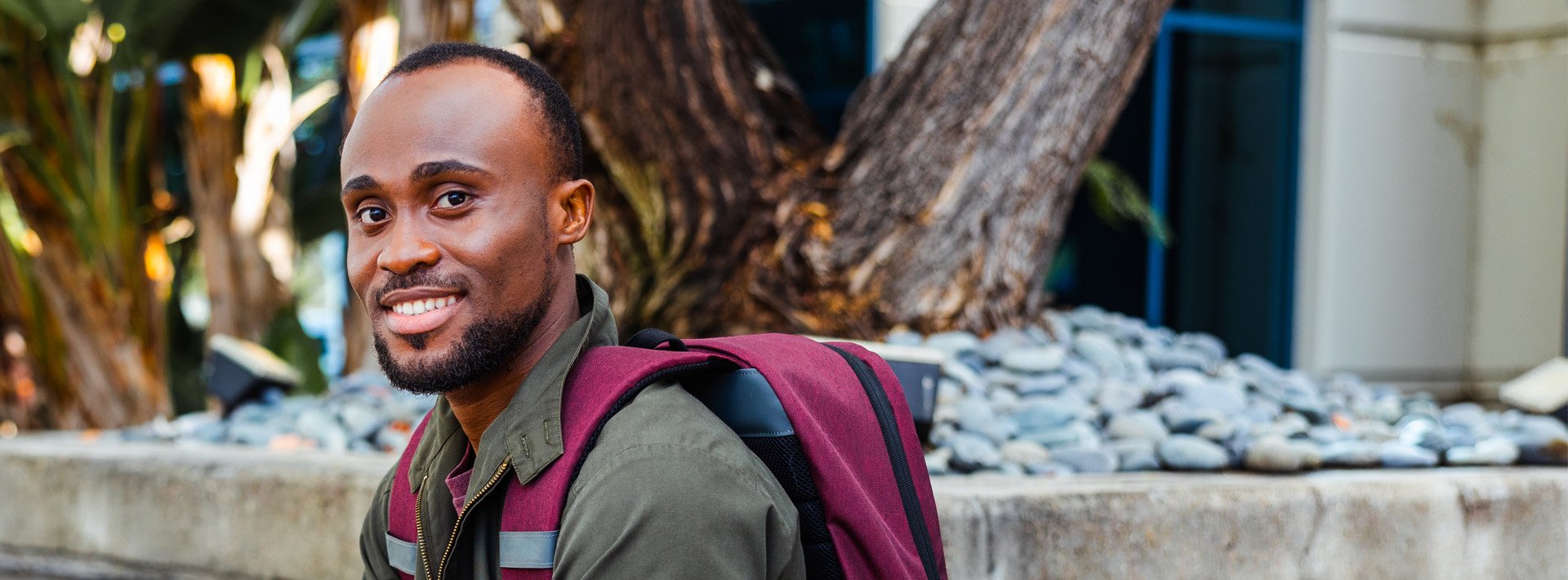 man sits outside with a backpack and smiles at the camera