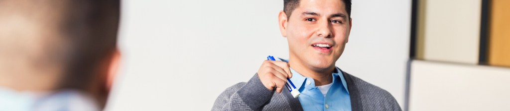 man holding whiteboard marker looking at a man across from him talking