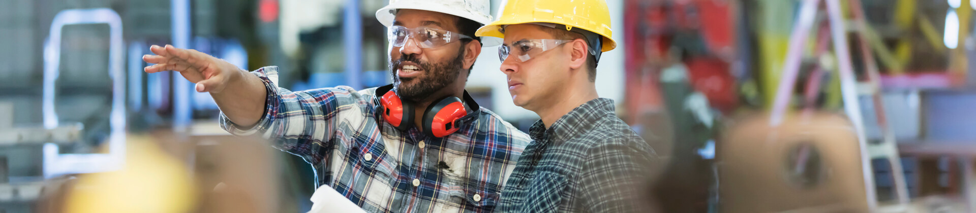 Two men in hard hats and safety glasses look at something out of frame for the Bachelor of Science in Construction Management Program Page
