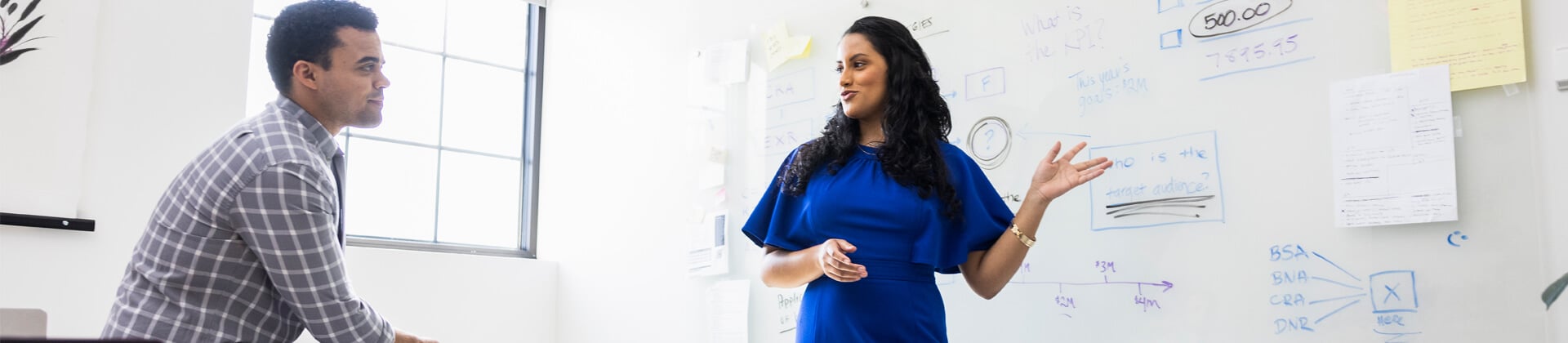 Woman stands in front of a whiteboard to explain a concept to the student, a man