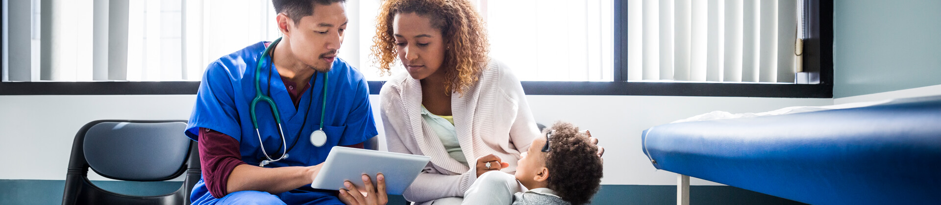 woman looks at a tablet with a medical professional while her young son looks on