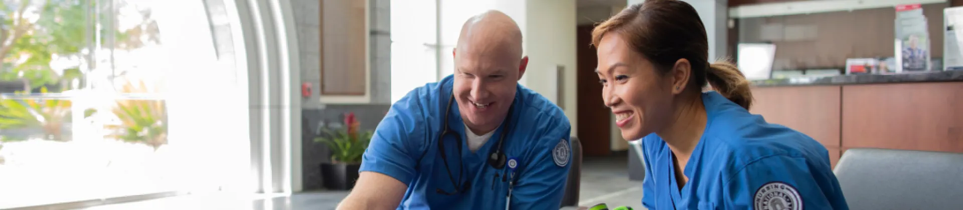 a White male and Asian woman medical professional students smile in lobby of campus