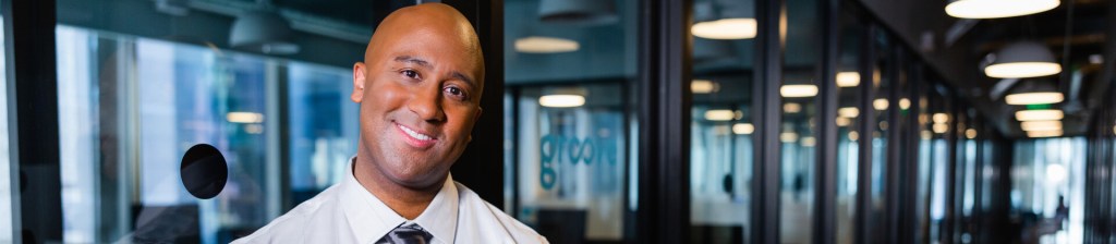 man in office hallway smiling into camera