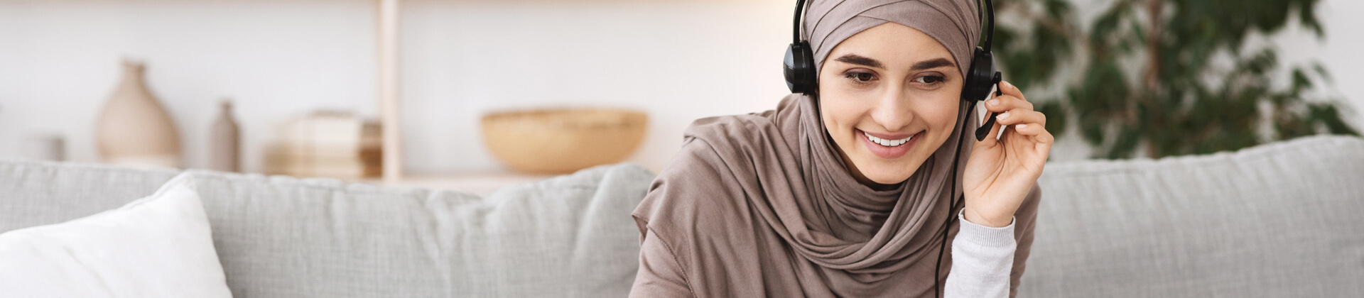 Woman in headscarf takes a call on a headset as she sits on a couch