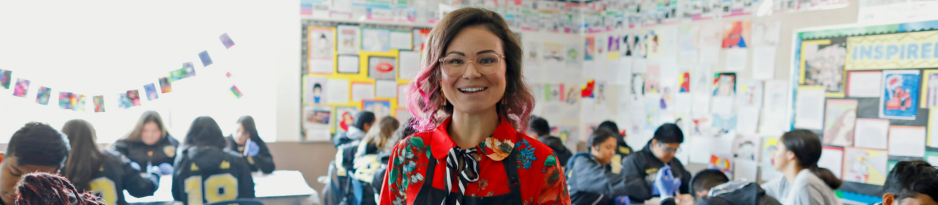 woman smiling at camera in classroom of adolescent students in background
