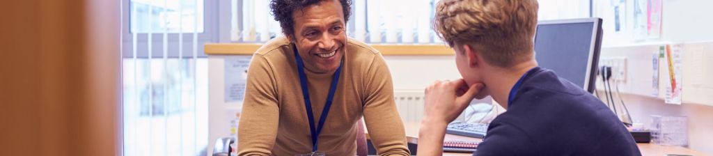 man sitting at desk smiling at adolescent boy facing him