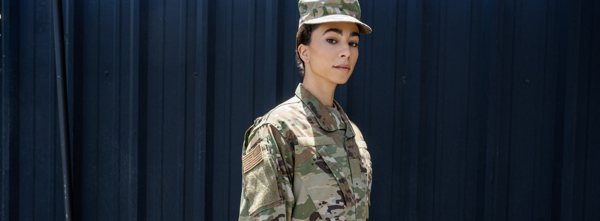 A woman in a military uniform stands in front of a dark background