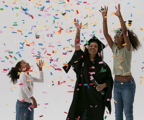 A recent grad in cap and gown throws confetti with her two children