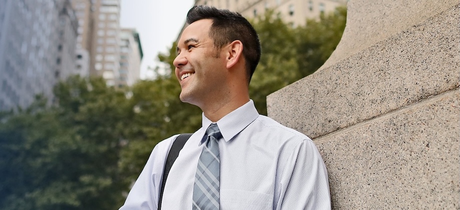 man leaning on wall wearing a tie and holding a tablet