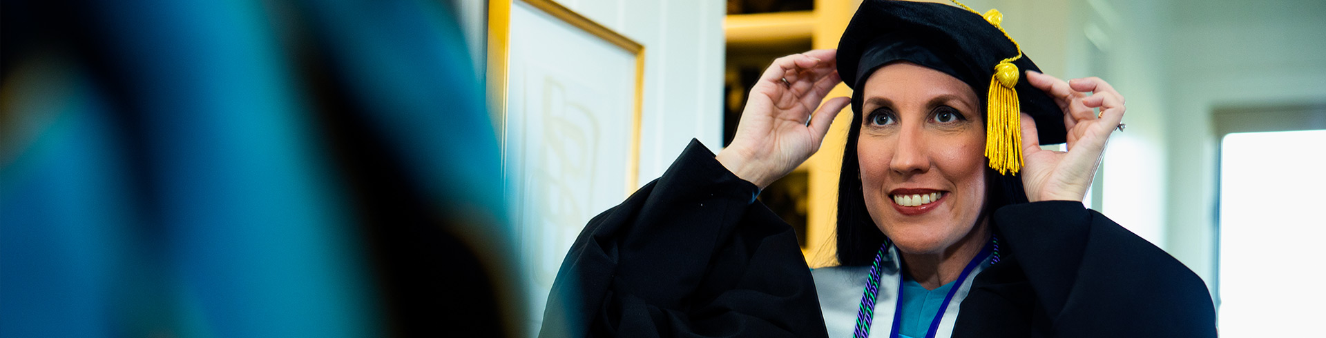 Graduate putting on cap and gown looking in mirror