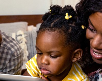 father and mother with toddler child between them looking at tablet