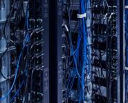 man kneeled down in server room looking up at rack holding tablet