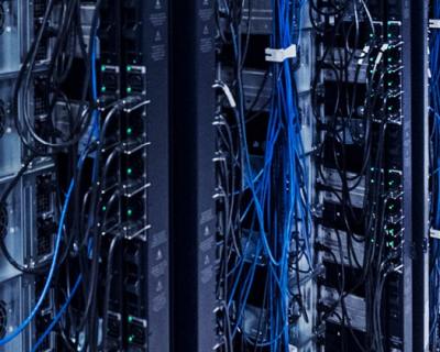 man kneeled down in server room looking up at rack holding tablet