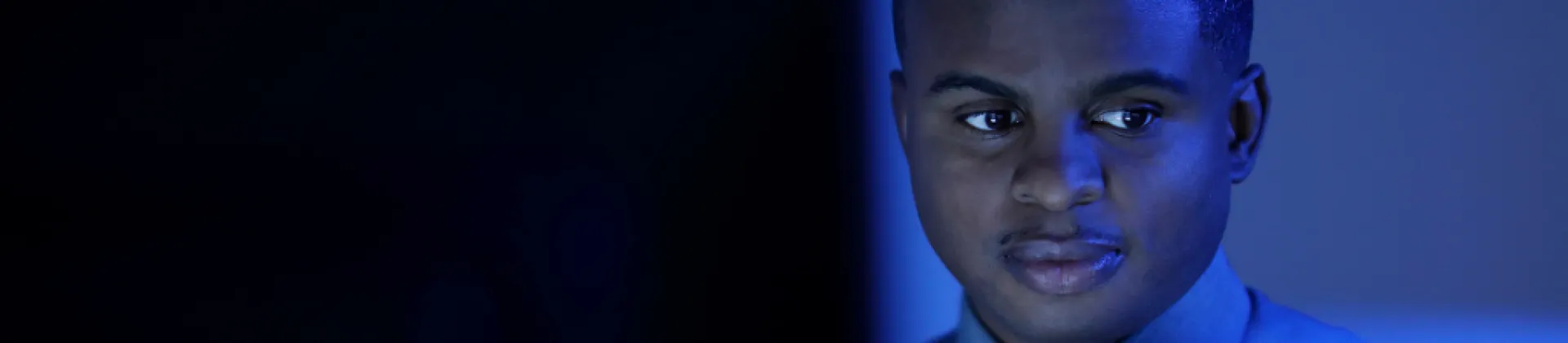 man in dark room lit up by computer screen working as a Penetration Tester looking to his left