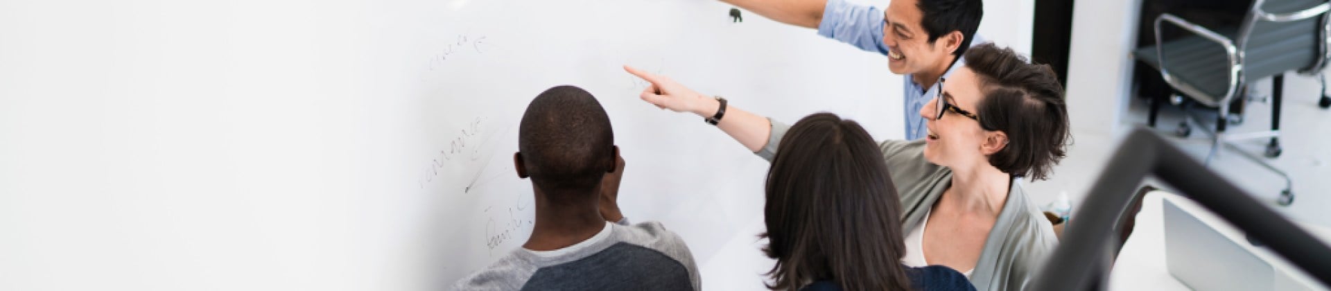 four individuals writing and pointing at whiteboard and smiling