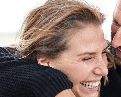 later middle aged couple smiling at the beach, woman's eyes are closed and man is looking down at her embracing her