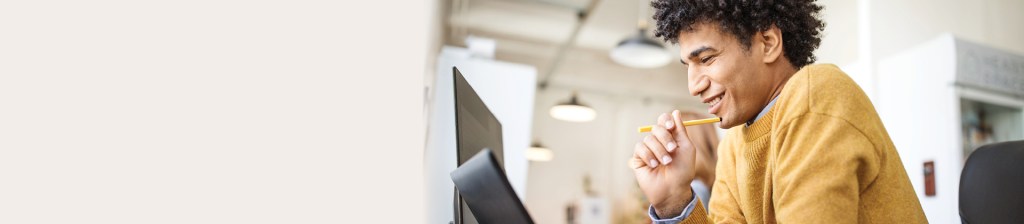 man looking down at laptop smiling while pen rests on his chin
