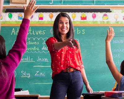 teacher in classroom with kids raising their hands