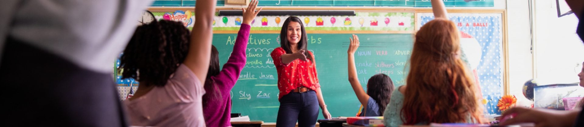 teacher in classroom with kids raising their hands