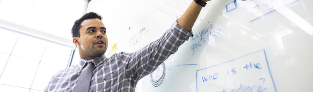 man with raised arm looking at whiteboard and pointing