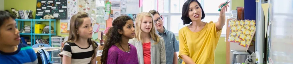 woman in a yellow top teaches a group of children in a classroom