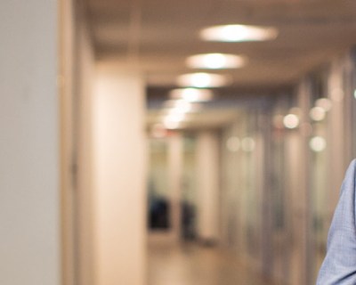 man with a beard in a gray suit smiles in a hallway