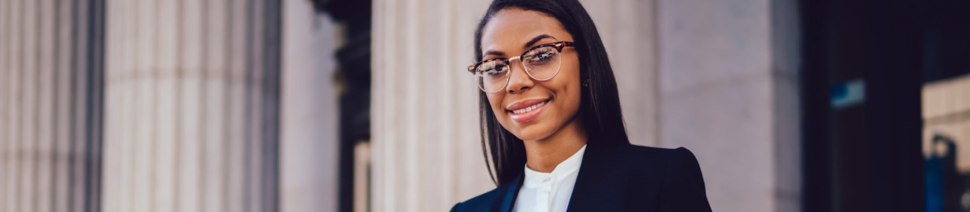 woman in glasses stands in front of a building